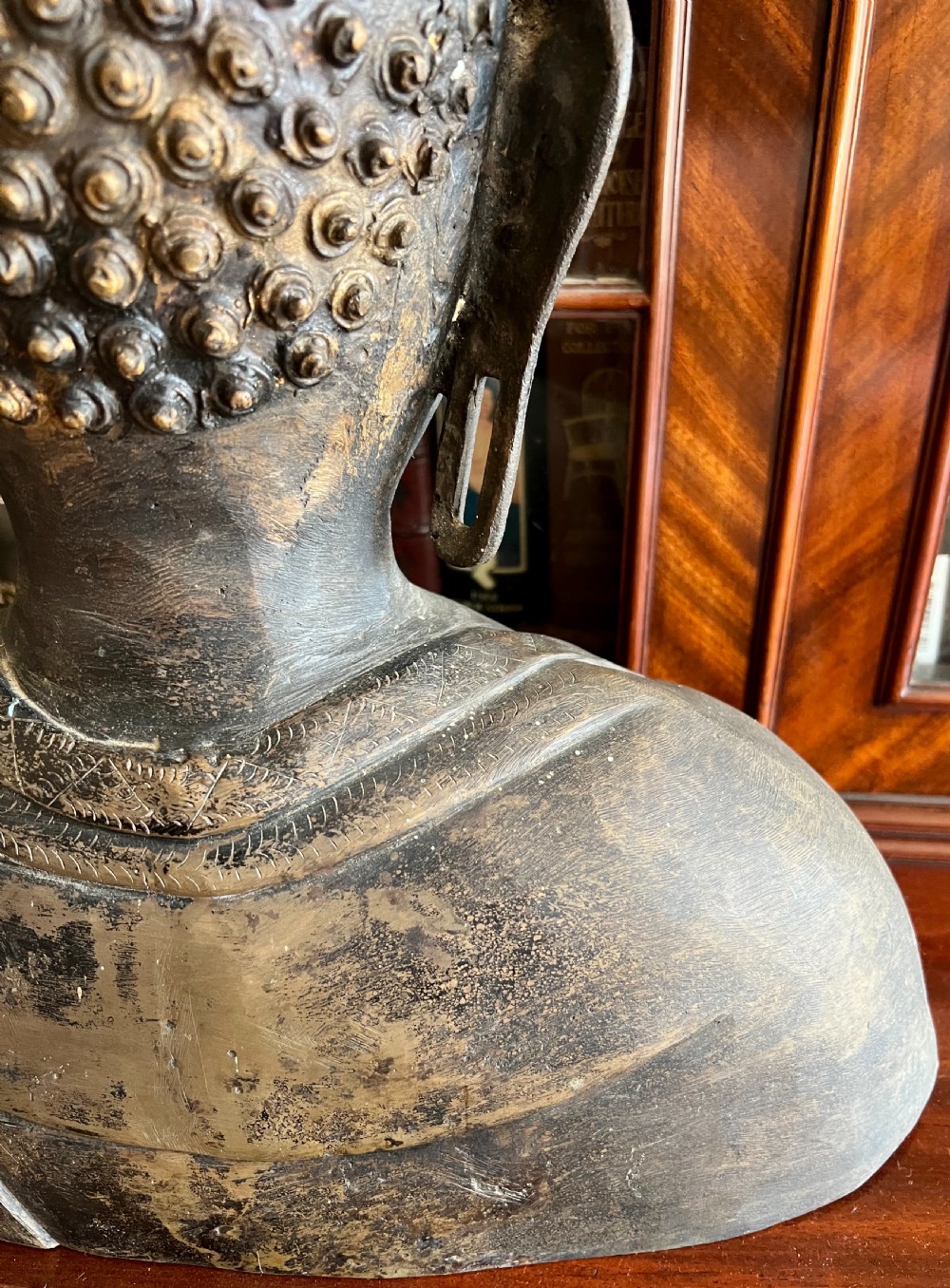 A cast bronze bust depicting a Buddha with downcast eyes, stylized hair curls, elongated earlobes, and draped robes. View VIII
