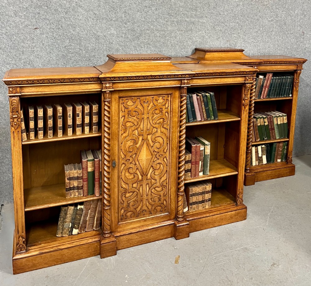 A pair of low oak open bookcases featuring raised central plinths, rope-twist columns, and intricately carved relief strapwork panels.