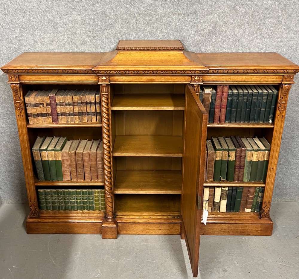 A pair of low oak open bookcases featuring raised central plinths, rope-twist columns, and intricately carved relief strapwork panels. View III