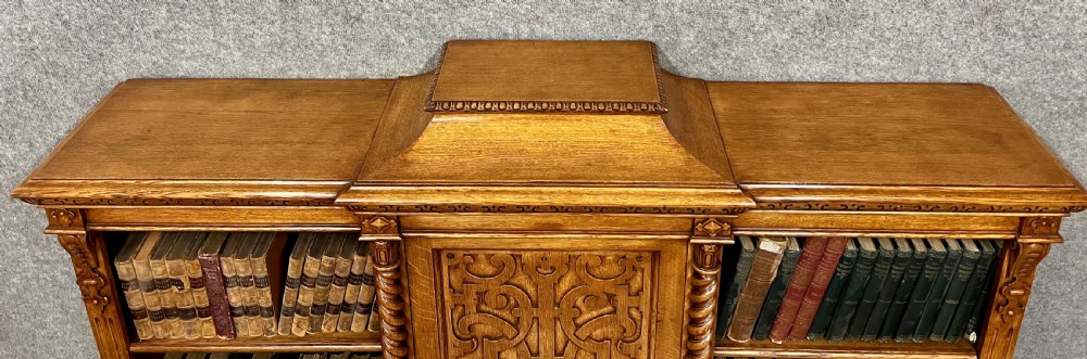 A pair of low oak open bookcases featuring raised central plinths, rope-twist columns, and intricately carved relief strapwork panels. View IV