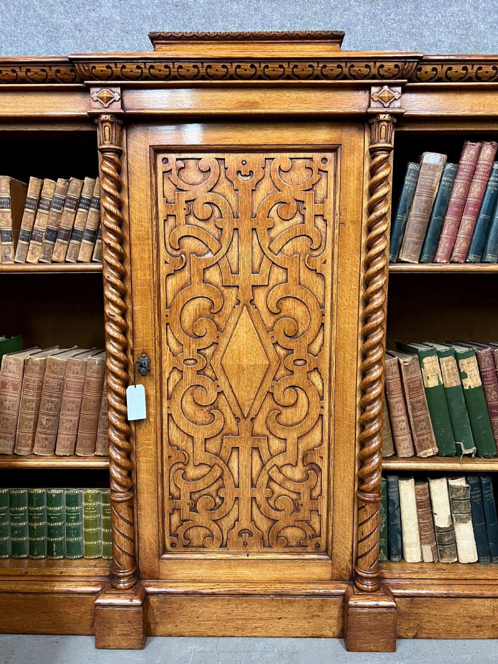 A pair of low oak open bookcases featuring raised central plinths, rope-twist columns, and intricately carved relief strapwork panels. View V