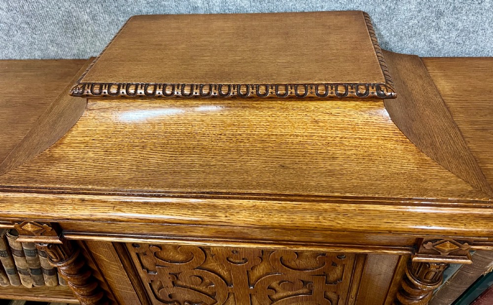 A pair of low oak open bookcases featuring raised central plinths, rope-twist columns, and intricately carved relief strapwork panels. View VIII