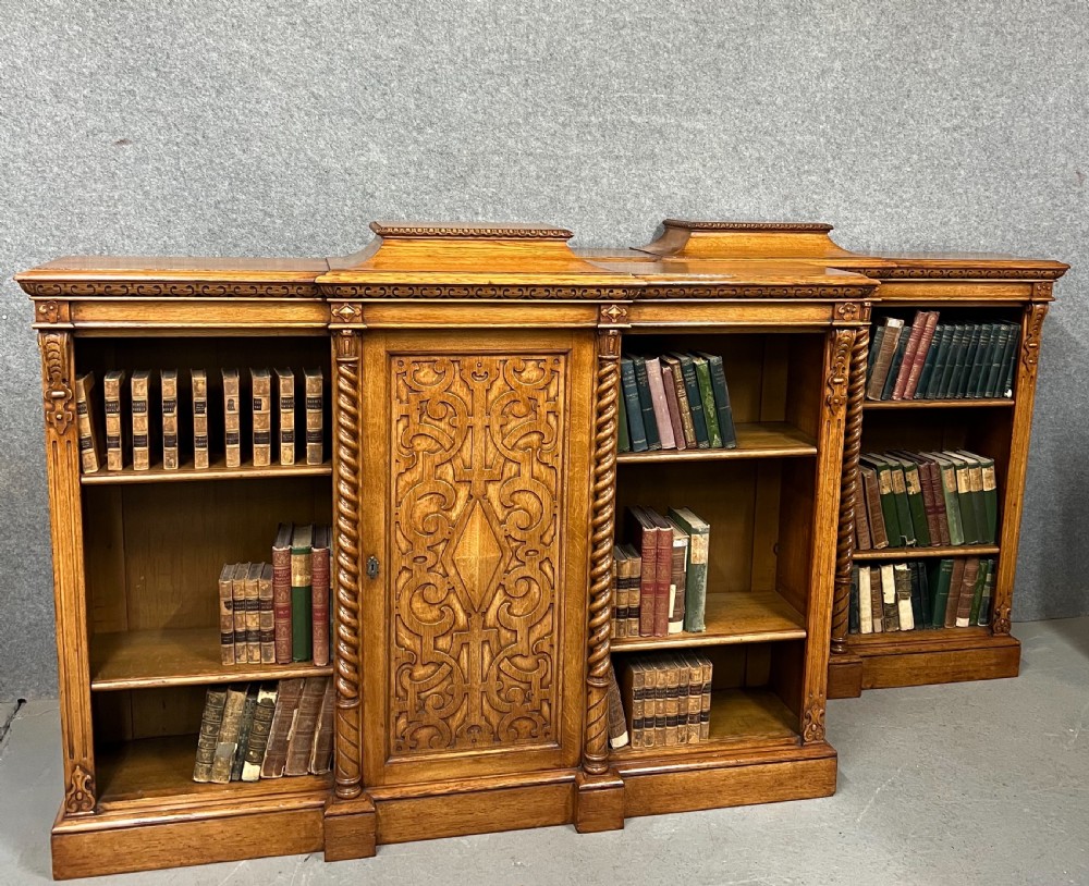 A pair of low oak open bookcases featuring raised central plinths, rope-twist columns, and intricately carved relief strapwork panels. View IX