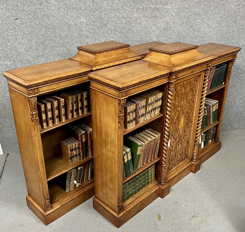 A pair of low oak open bookcases featuring raised central plinths, rope-twist columns, and intricately carved relief strapwork panels. View X