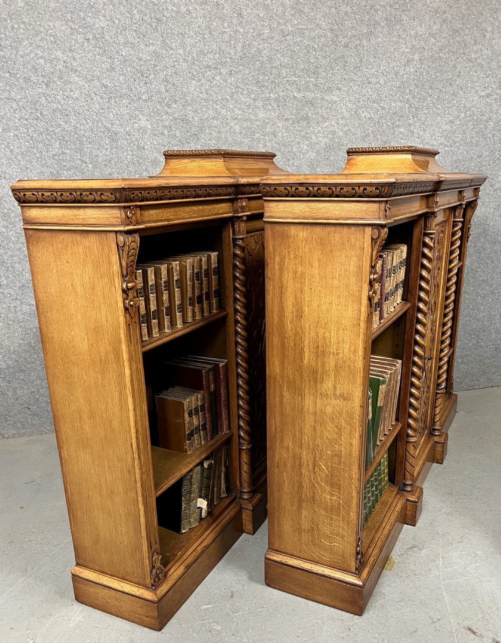 A pair of low oak open bookcases featuring raised central plinths, rope-twist columns, and intricately carved relief strapwork panels. View XI