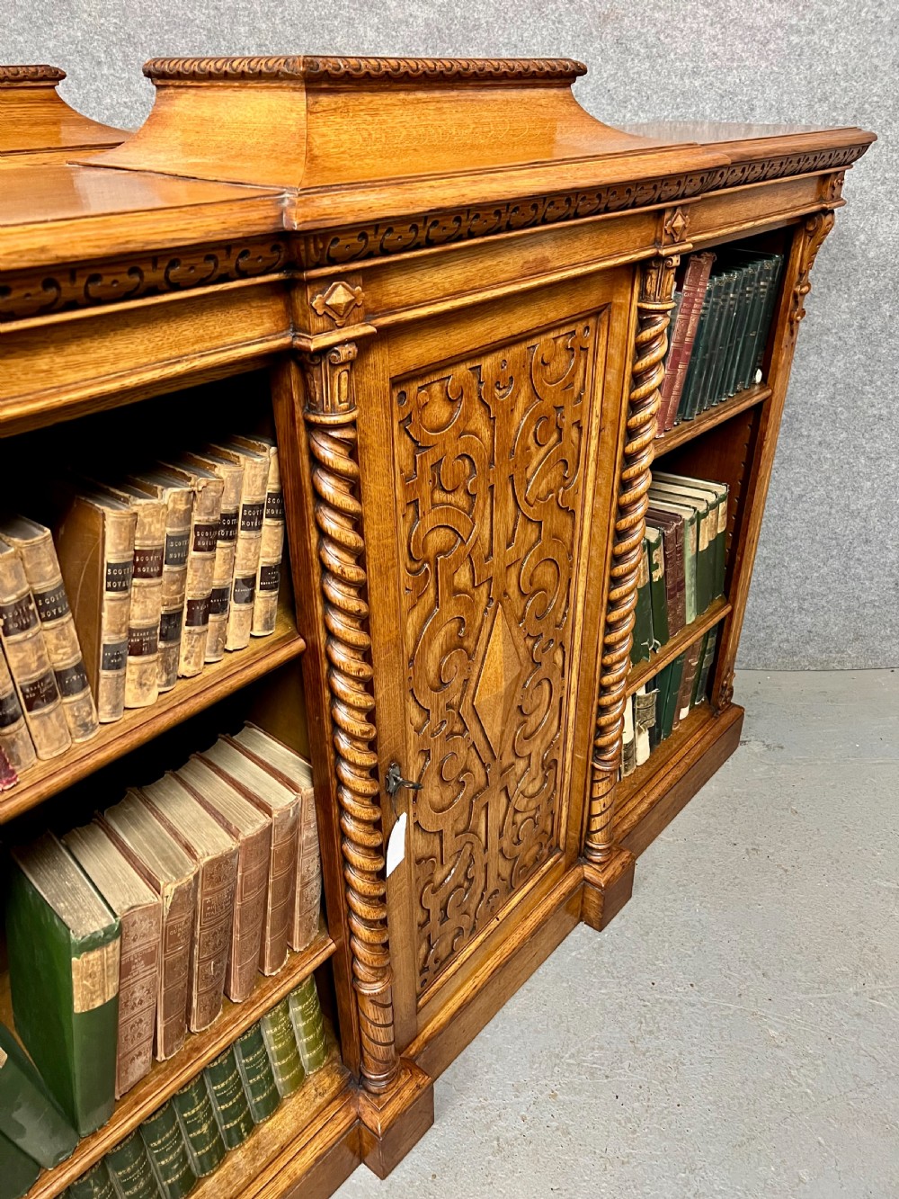 A pair of low oak open bookcases featuring raised central plinths, rope-twist columns, and intricately carved relief strapwork panels. View XIII