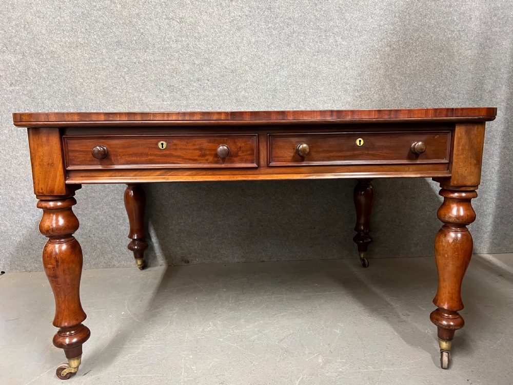 A Victorian mahogany writing table featuring a green leather inset top with gold tooling, two frieze drawers, and turned legs on brass castors. View XII