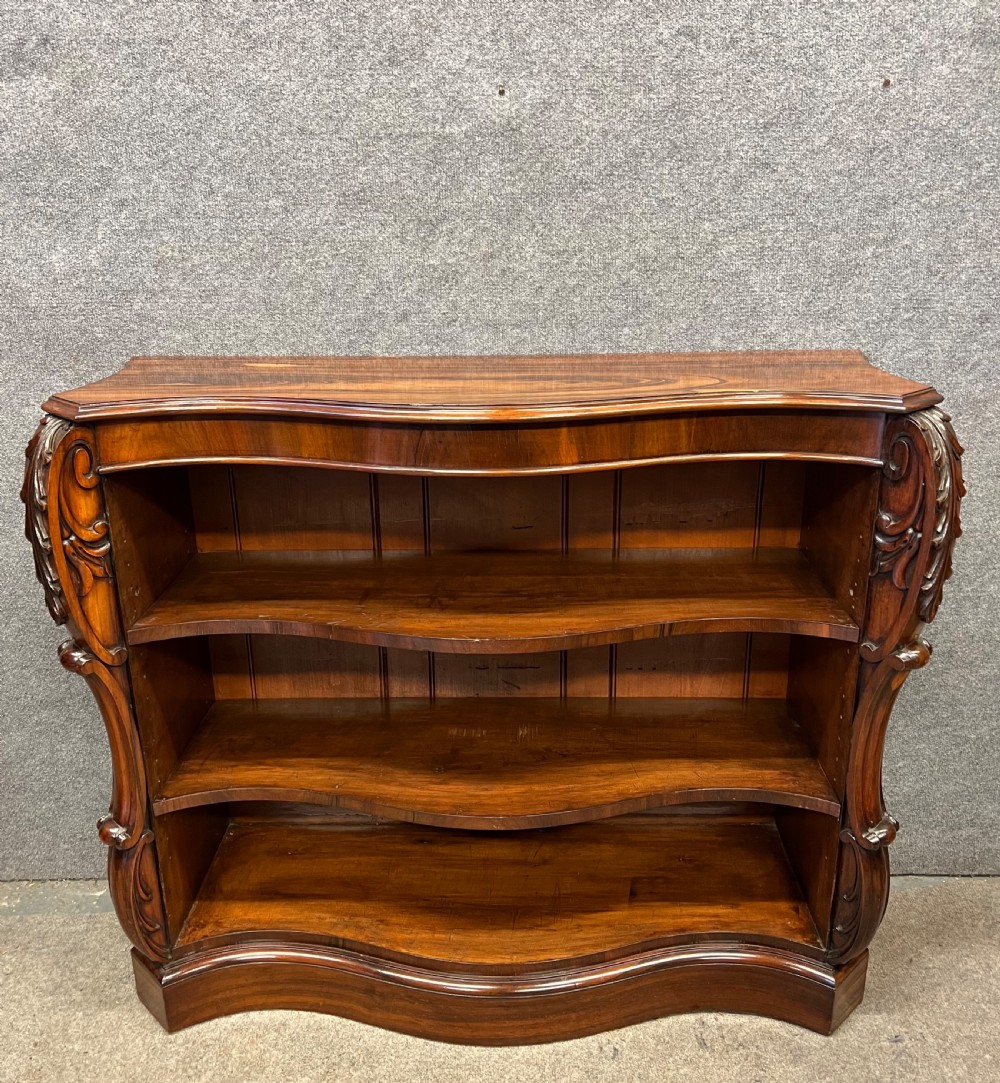 A low nineteenth-century open bookcase crafted from Goncalo Alves wood, featuring serpentine front shelves and carved acanthus leaf corbels. View II