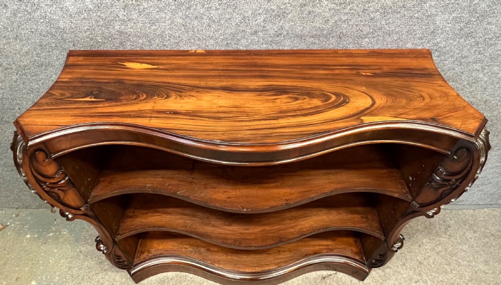 A low nineteenth-century open bookcase crafted from Goncalo Alves wood, featuring serpentine front shelves and carved acanthus leaf corbels. View VII