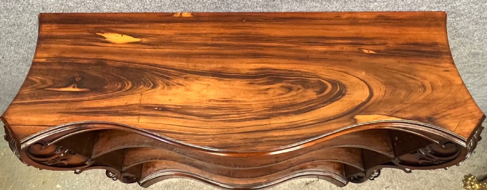 A low nineteenth-century open bookcase crafted from Goncalo Alves wood, featuring serpentine front shelves and carved acanthus leaf corbels. View VIII