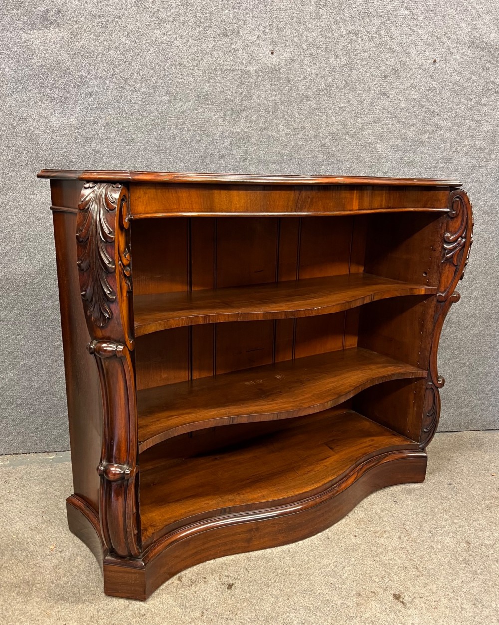 A low nineteenth-century open bookcase crafted from Goncalo Alves wood, featuring serpentine front shelves and carved acanthus leaf corbels. View XI