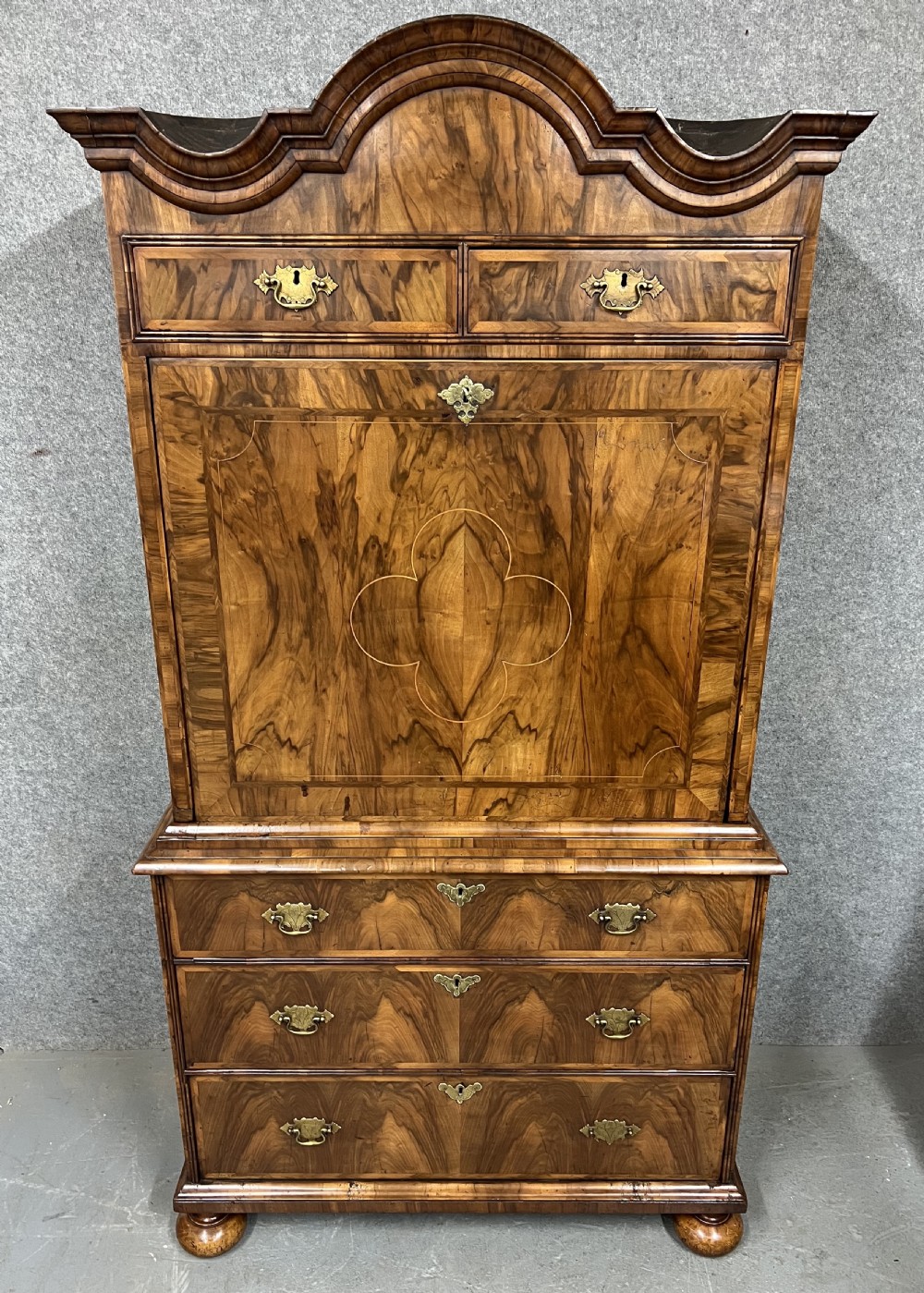 A William and Mary figured walnut escritoire featuring a double-dome arched pediment, a fall-front writing surface concealing a multi-drawer fitted interior, and a chest base on turned bun feet. View II