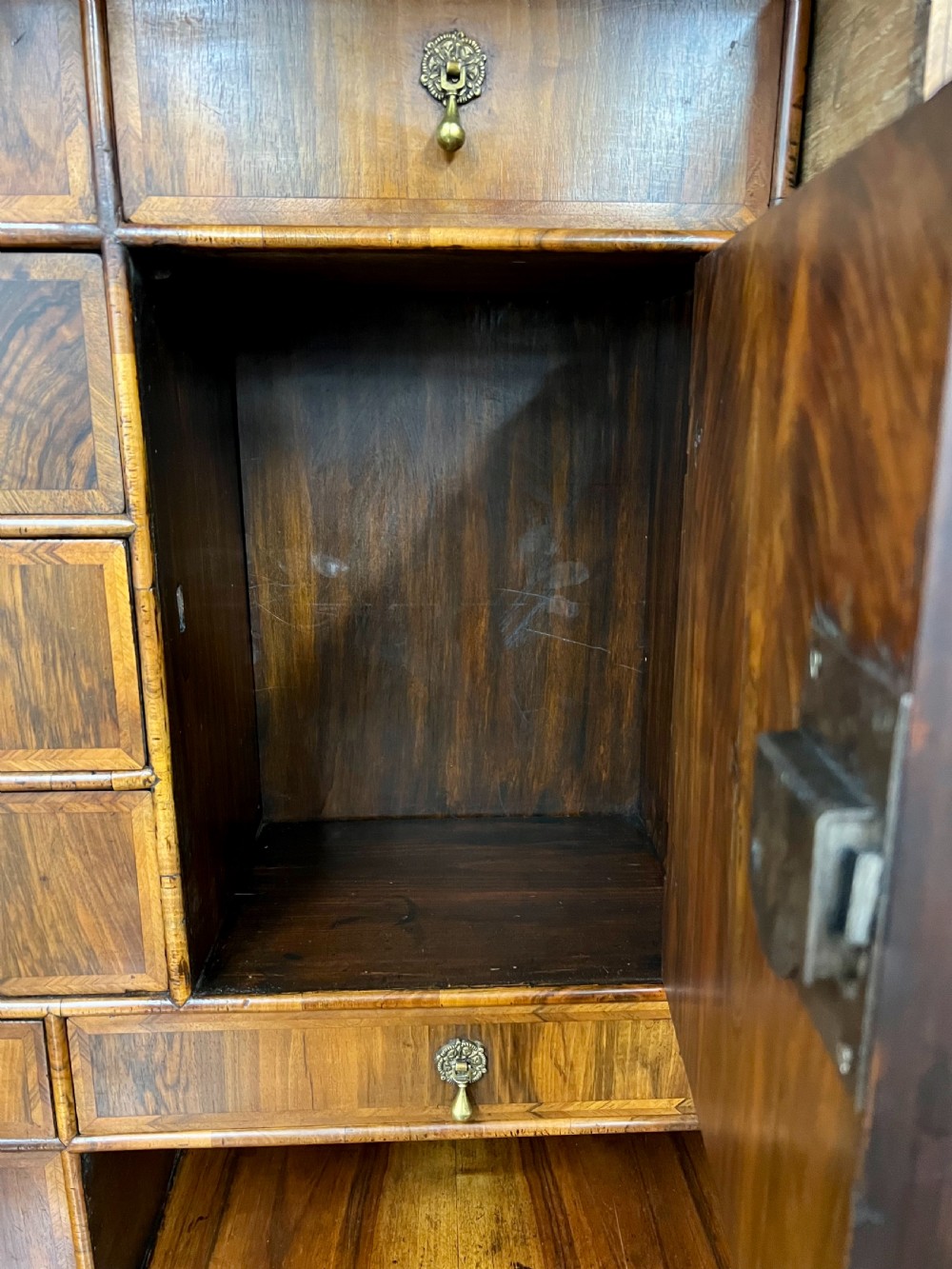 A William and Mary figured walnut escritoire featuring a double-dome arched pediment, a fall-front writing surface concealing a multi-drawer fitted interior, and a chest base on turned bun feet. View V