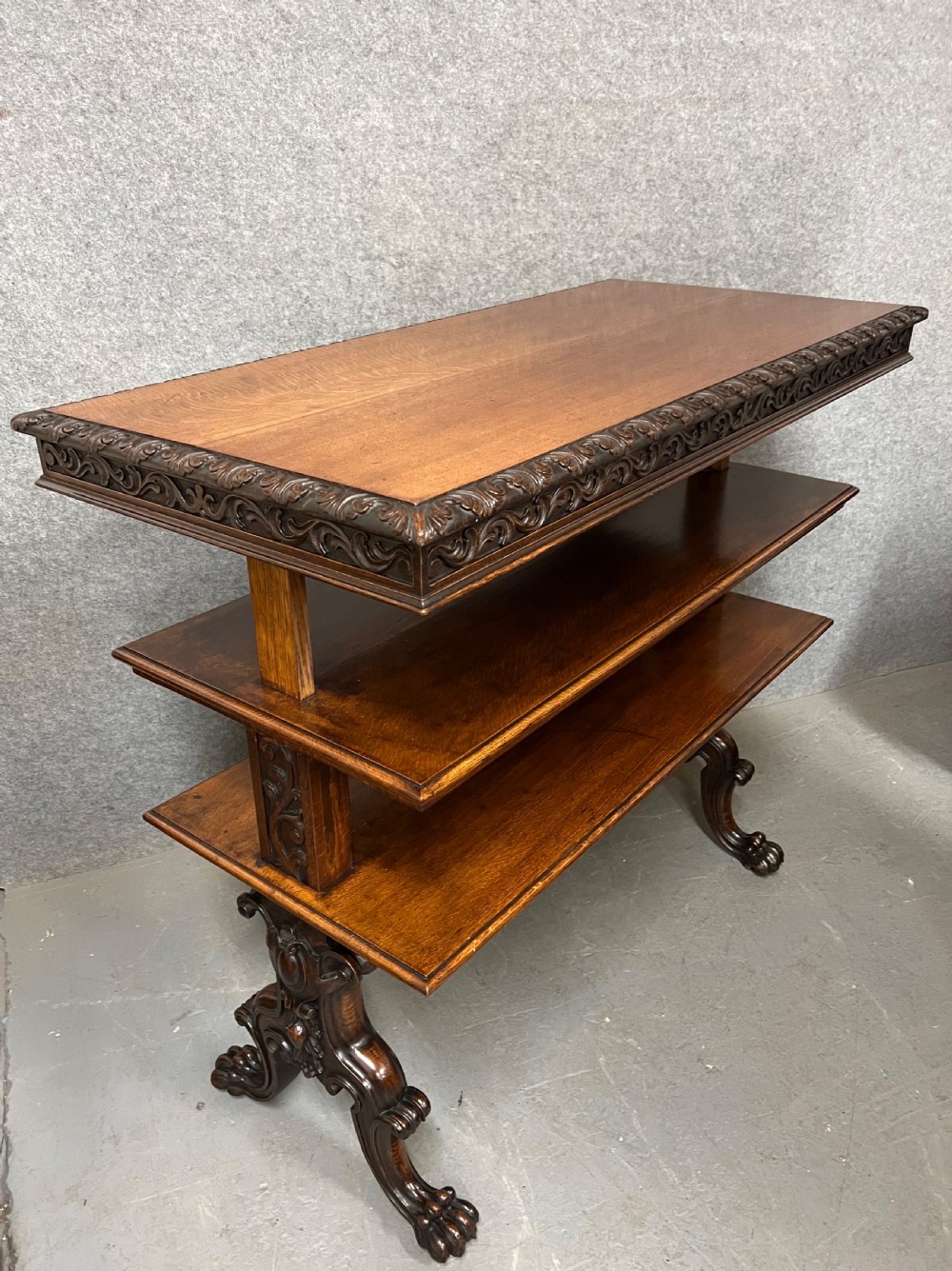 A dark oak Victorian rise and fall three-tiered dumb waiter with carved foliage borders and ornate leg supports.