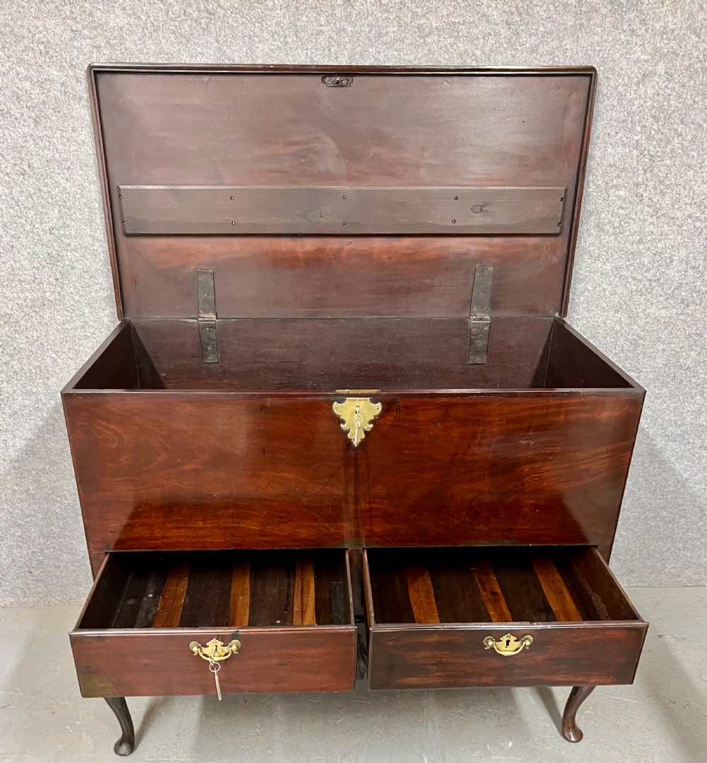 A George II mahogany chest on stand featuring a hinged top, two lower drawers with brass keyplates, a central carved shell apron, and cabriole legs. View II