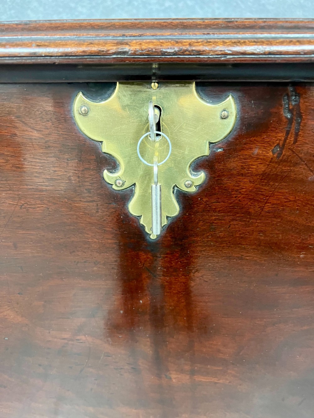 A George II mahogany chest on stand featuring a hinged top, two lower drawers with brass keyplates, a central carved shell apron, and cabriole legs. View V