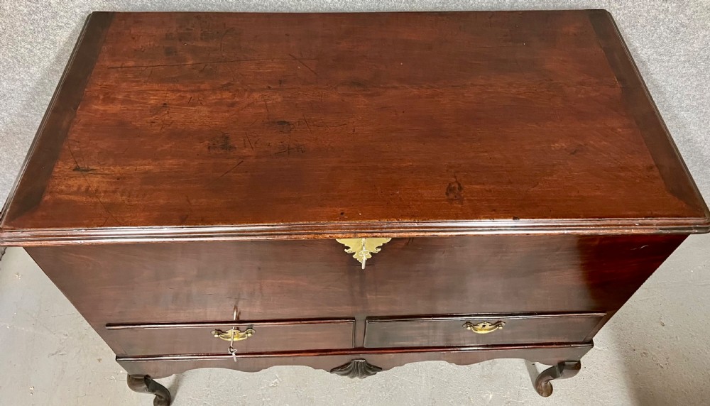 A George II mahogany chest on stand featuring a hinged top, two lower drawers with brass keyplates, a central carved shell apron, and cabriole legs. View VII