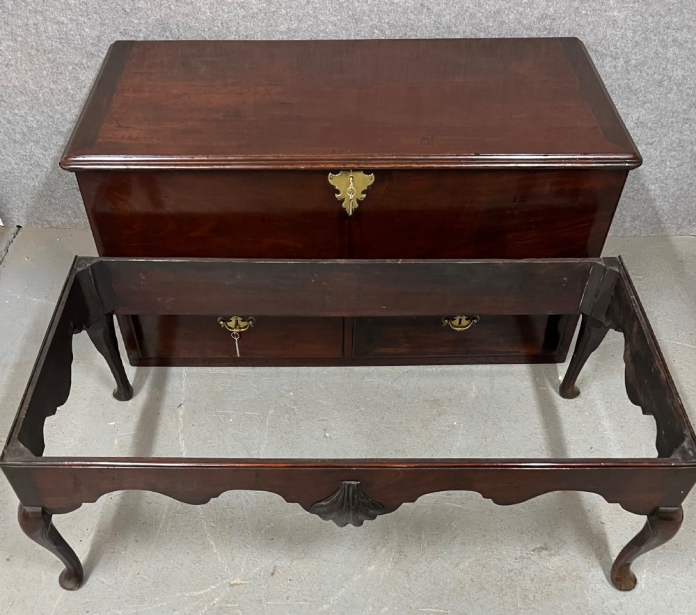 A George II mahogany chest on stand featuring a hinged top, two lower drawers with brass keyplates, a central carved shell apron, and cabriole legs. View IX