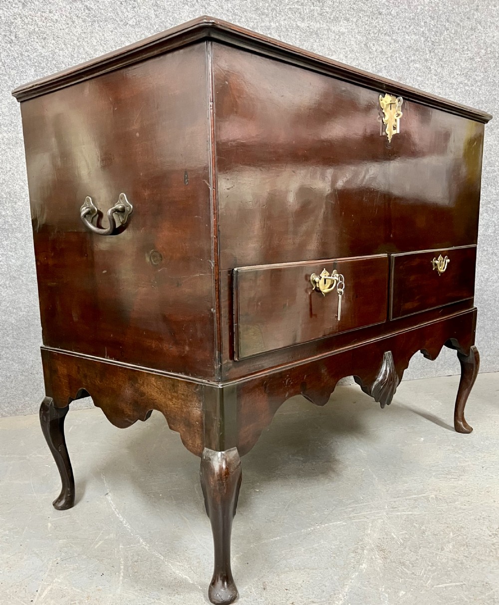 A George II mahogany chest on stand featuring a hinged top, two lower drawers with brass keyplates, a central carved shell apron, and cabriole legs. View X