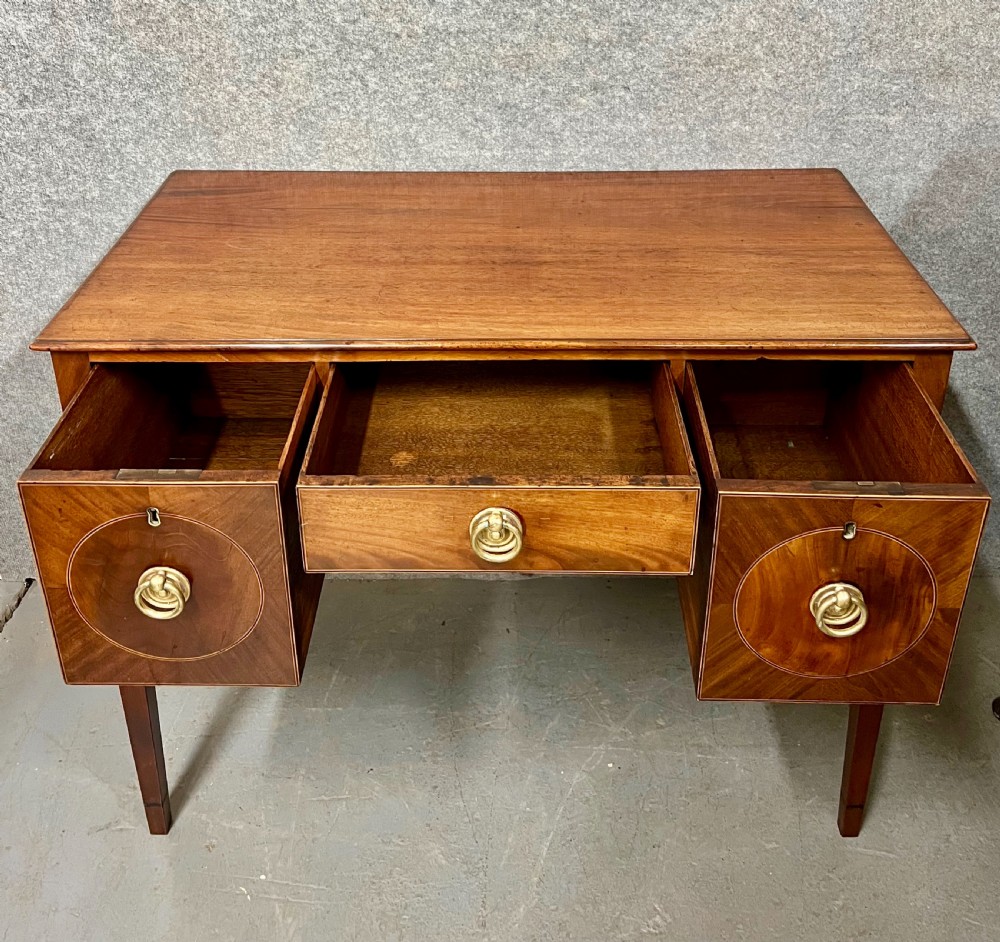 A small Georgian mahogany sideboard featuring three drawers with circular veneered panels, brass ring handles, and four square tapered legs. View V