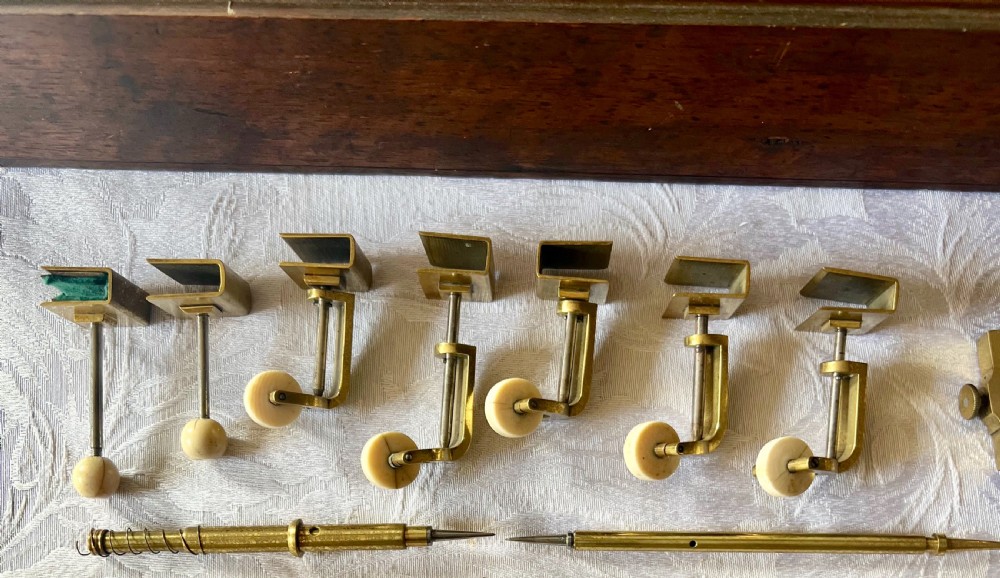 An antique brass pantograph with various small attachments laid out alongside its open fitted mahogany case with green felt lining. View II