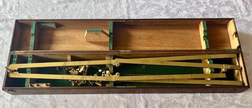 An antique brass pantograph with various small attachments laid out alongside its open fitted mahogany case with green felt lining. View III