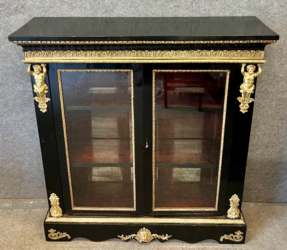 An ebonised two-door display cabinet featuring glass panels, detailed gilt bronze ormolu mounts, cherub term figures, and ornamental friezes. View II