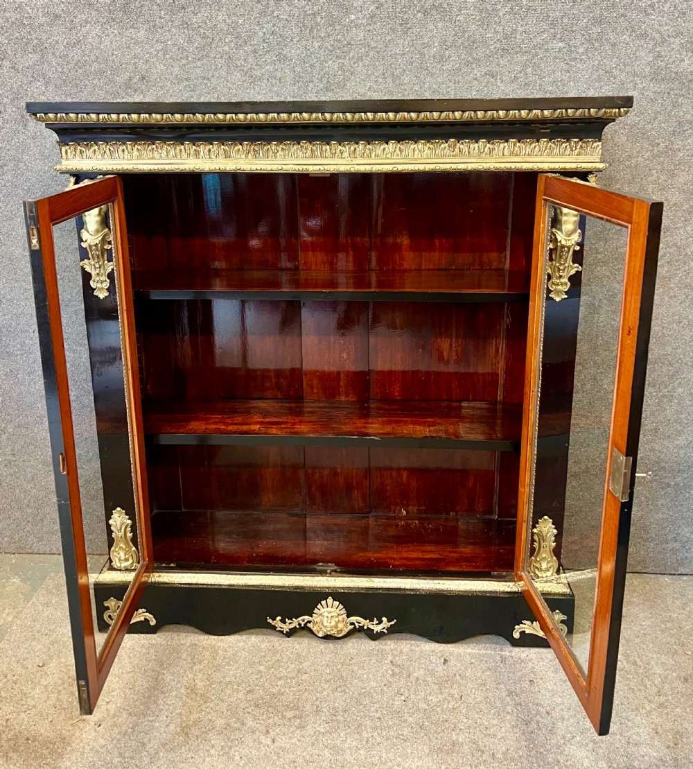 An ebonised two-door display cabinet featuring glass panels, detailed gilt bronze ormolu mounts, cherub term figures, and ornamental friezes. View IX