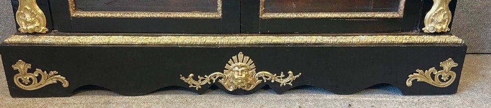 An ebonised two-door display cabinet featuring glass panels, detailed gilt bronze ormolu mounts, cherub term figures, and ornamental friezes. View X