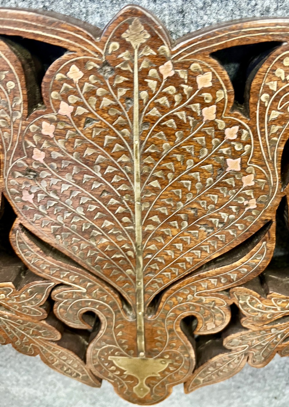 An Anglo-Indian X-frame Savonarola armchair crafted from dark carved wood featuring intricate brass inlay depicting peacocks and foliage with carved animal head armrests. View IV