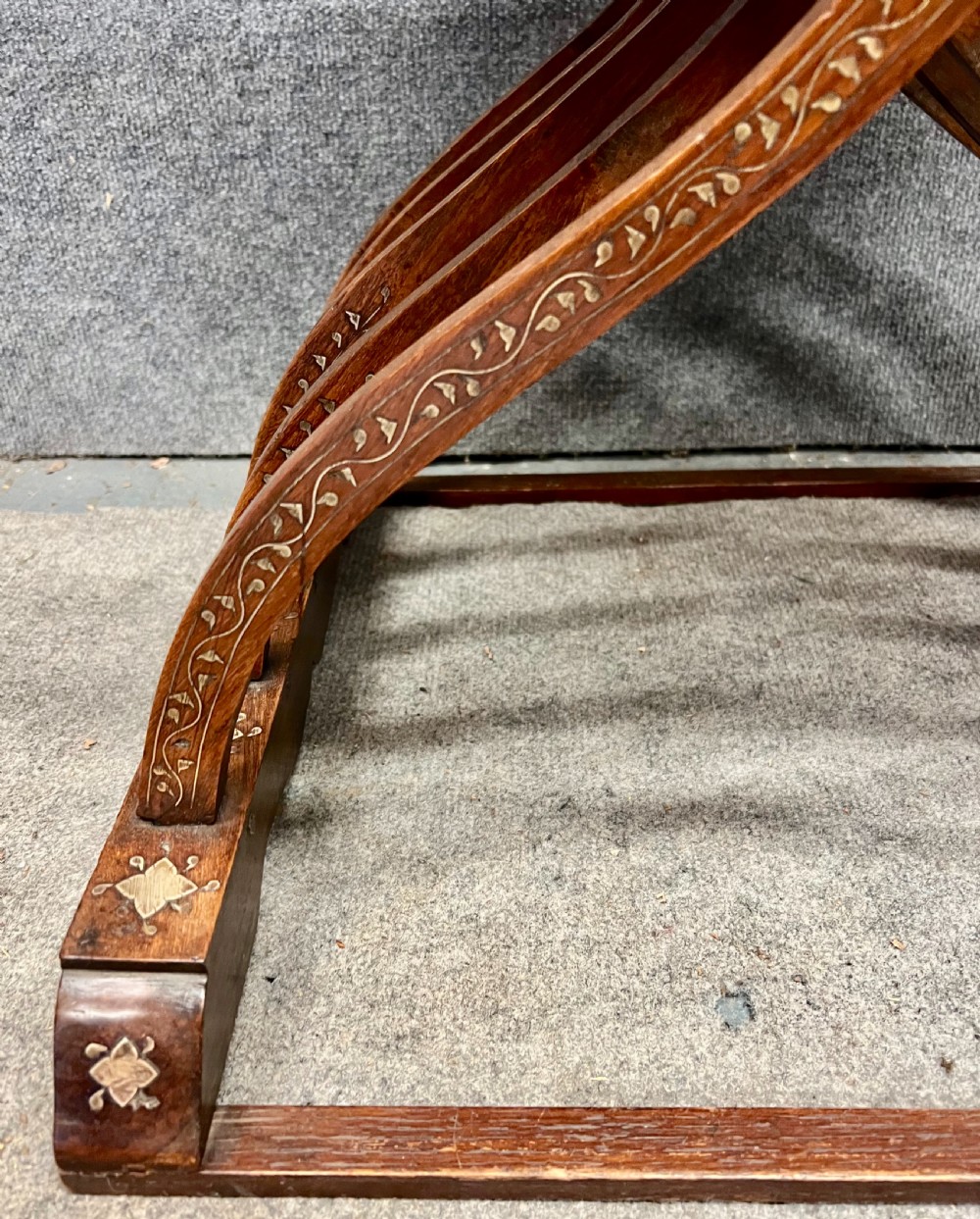 An Anglo-Indian X-frame Savonarola armchair crafted from dark carved wood featuring intricate brass inlay depicting peacocks and foliage with carved animal head armrests. View XI