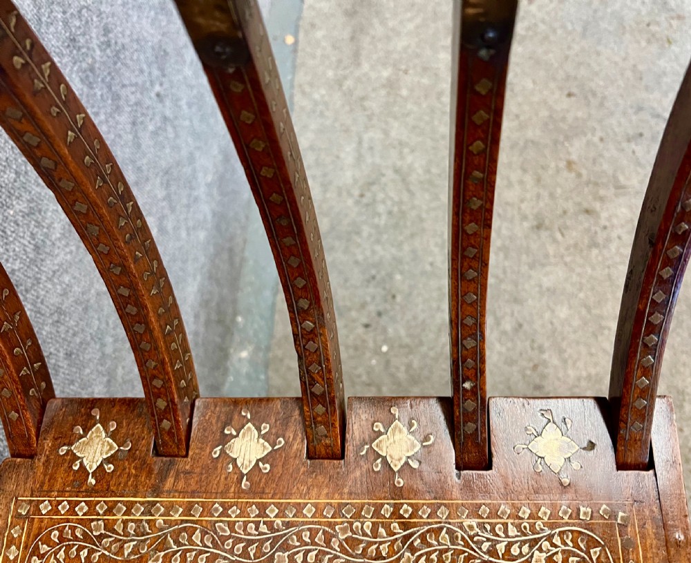 An Anglo-Indian X-frame Savonarola armchair crafted from dark carved wood featuring intricate brass inlay depicting peacocks and foliage with carved animal head armrests. View XIII