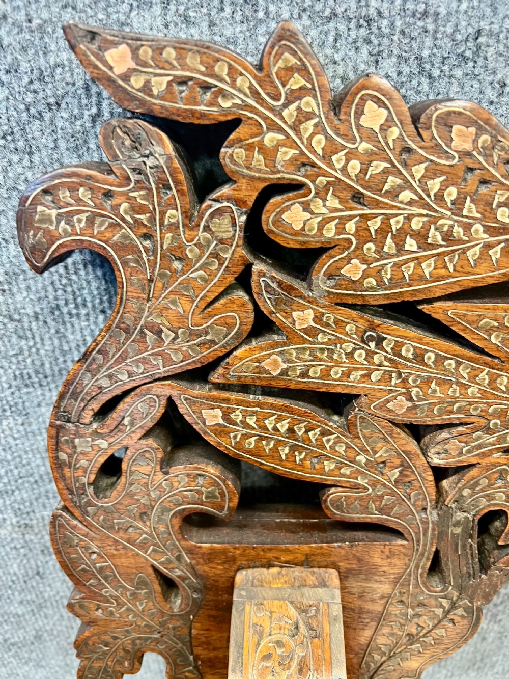 An Anglo-Indian X-frame Savonarola armchair crafted from dark carved wood featuring intricate brass inlay depicting peacocks and foliage with carved animal head armrests. View XIV