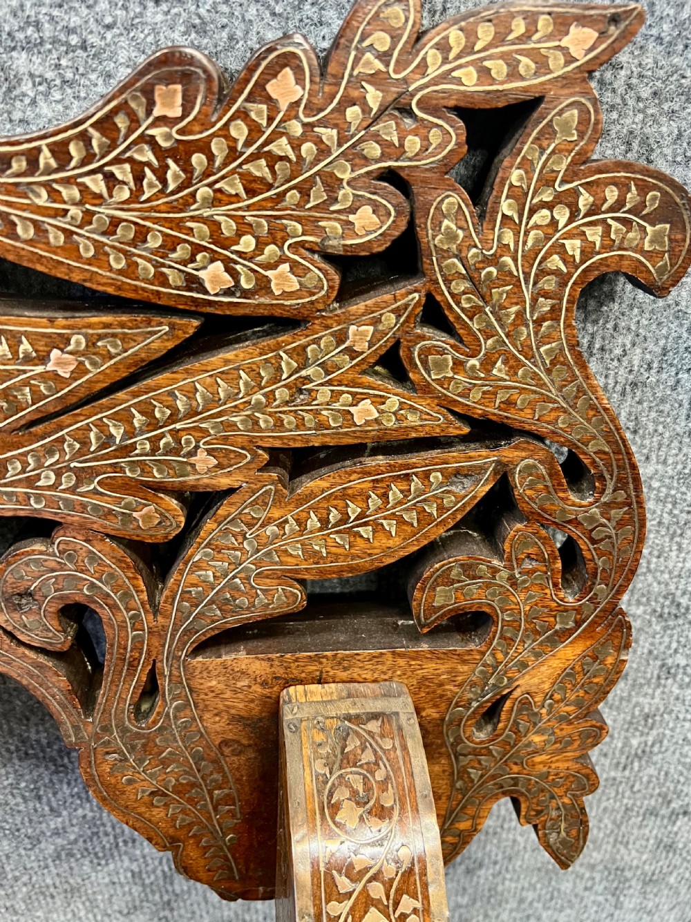 An Anglo-Indian X-frame Savonarola armchair crafted from dark carved wood featuring intricate brass inlay depicting peacocks and foliage with carved animal head armrests. View XV