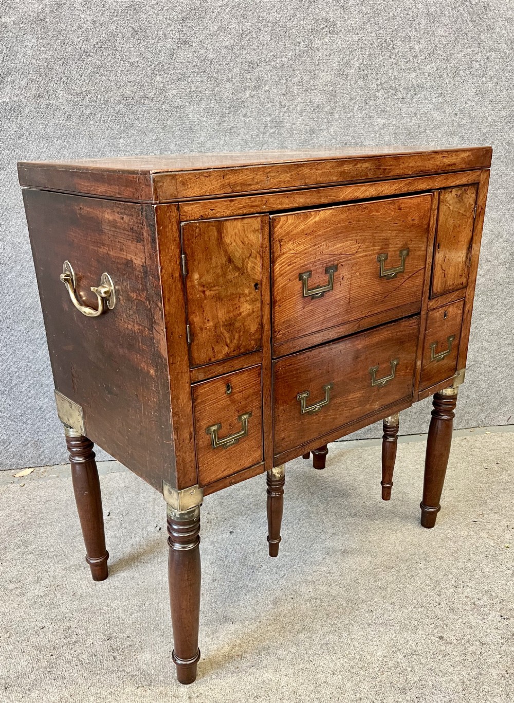 A George III mahogany campaign dressing chest featuring a hinged top revealing an adjustable mirror, brass corner mounts, flush handles, and turned legs. View II