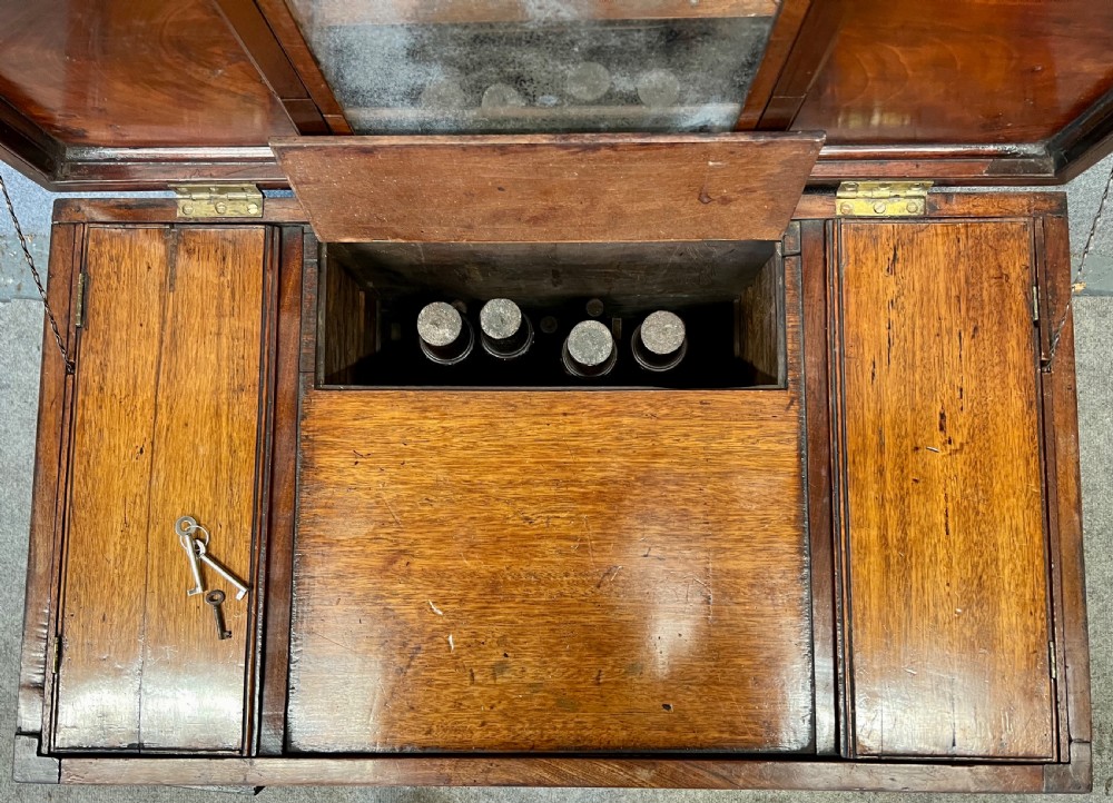 A George III mahogany campaign dressing chest featuring a hinged top revealing an adjustable mirror, brass corner mounts, flush handles, and turned legs. View V