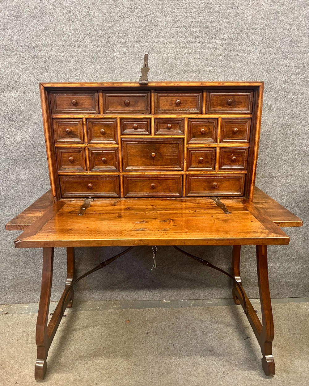A 17th-century Spanish walnut Vargueno cabinet with an open drop-front writing flap revealing multiple fitted drawers, set on a trestle stand with iron stretchers.