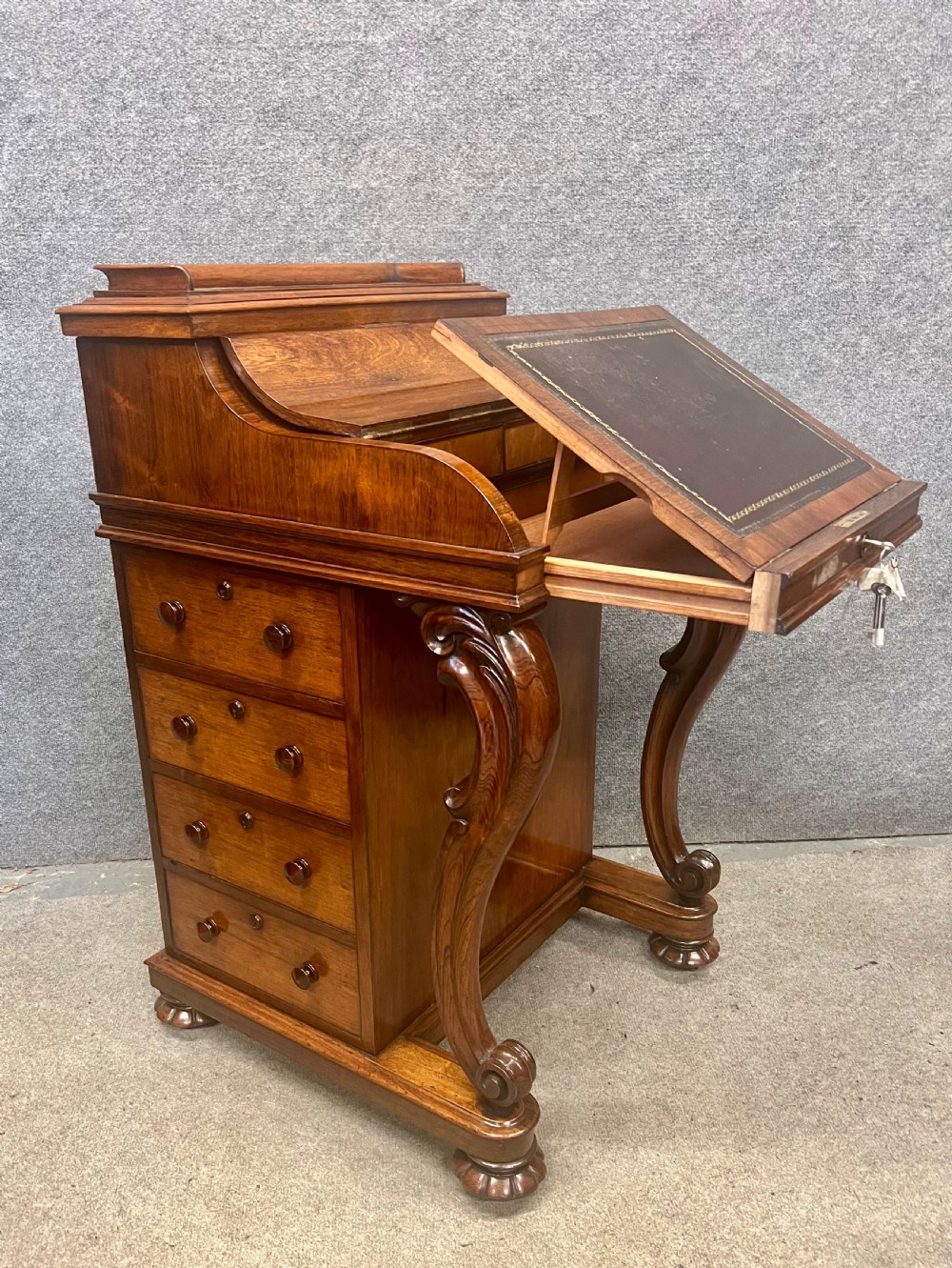 A Victorian rosewood davenport desk with an elevated pop-up stationery gallery, slanted piano top writing slope, side drawers, and carved cabriole support legs. View IV