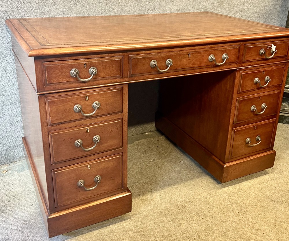 Late Victorian mahogany pedestal desk featuring a brown leather-tooled writing surface, nine drawers with brass handles, and twin pedestals on hidden castors. View II