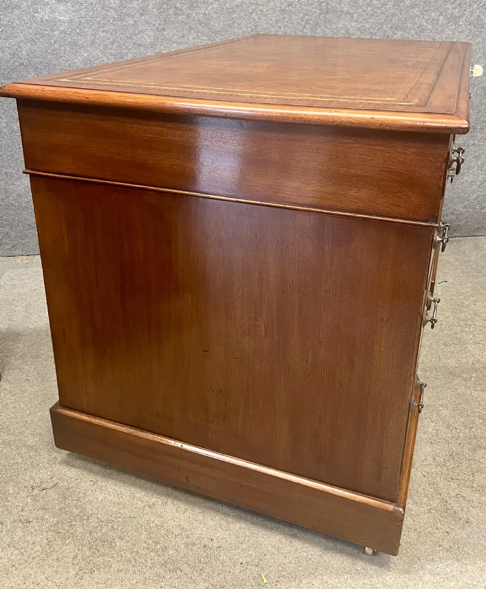 Late Victorian mahogany pedestal desk featuring a brown leather-tooled writing surface, nine drawers with brass handles, and twin pedestals on hidden castors. View VI