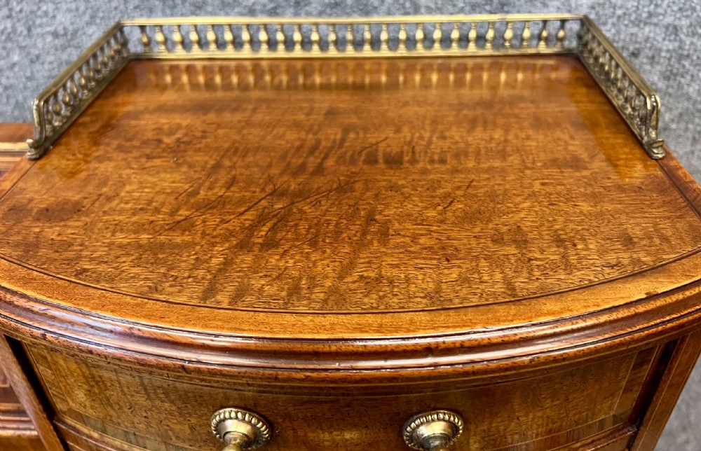 An antique mahogany Carlton House desk featuring satinwood inlay, a green leather writing surface, small raised drawers with brass gallery railings, and square tapered legs on castors. View XI