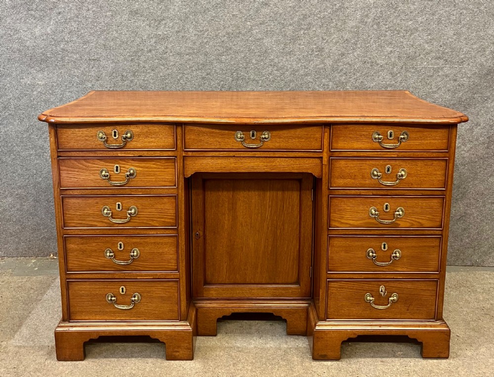 A George III mahogany kneehole desk featuring multiple drawers with brass swan-neck handles, a central recessed cupboard, and bracket feet.