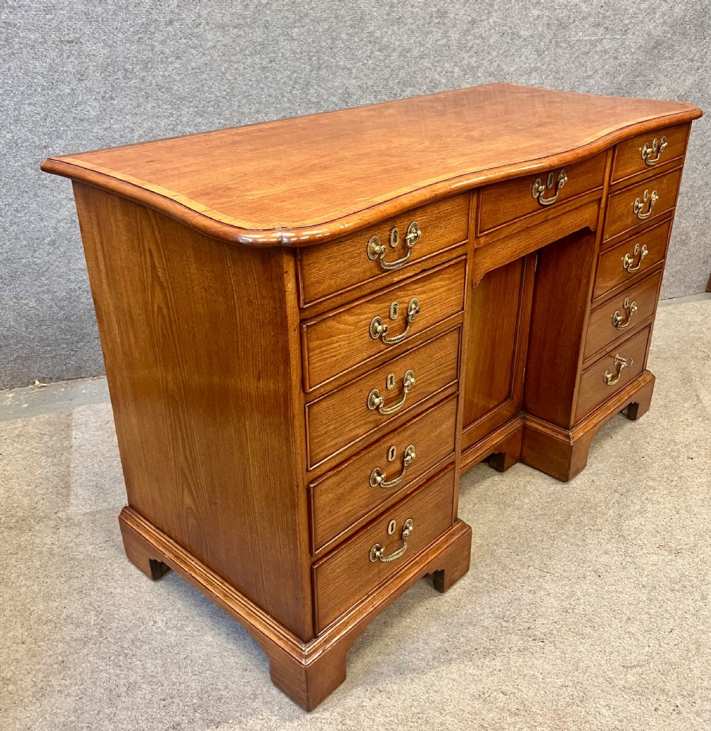 A George III mahogany kneehole desk featuring multiple drawers with brass swan-neck handles, a central recessed cupboard, and bracket feet. View II