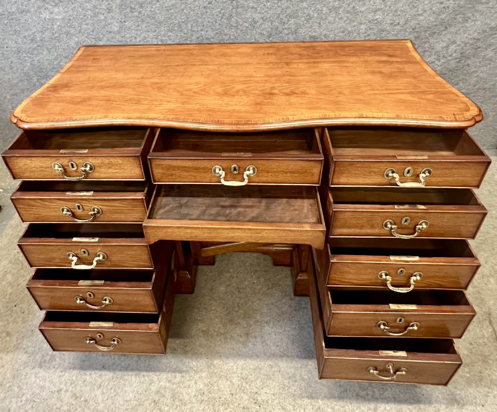 A George III mahogany kneehole desk featuring multiple drawers with brass swan-neck handles, a central recessed cupboard, and bracket feet. View V