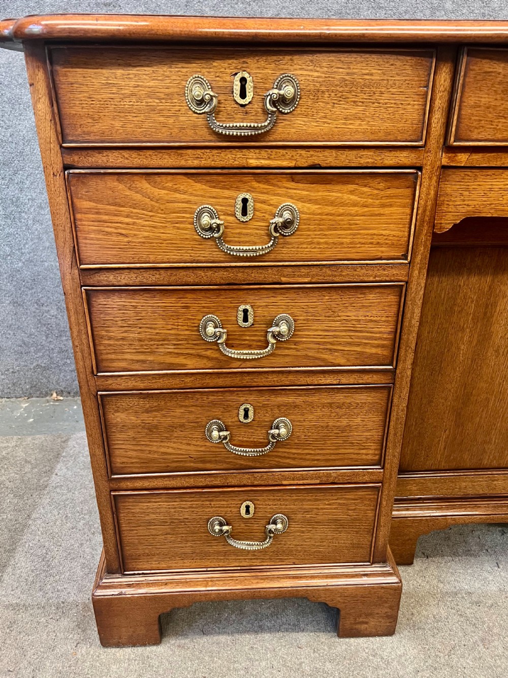 A George III mahogany kneehole desk featuring multiple drawers with brass swan-neck handles, a central recessed cupboard, and bracket feet. View VII