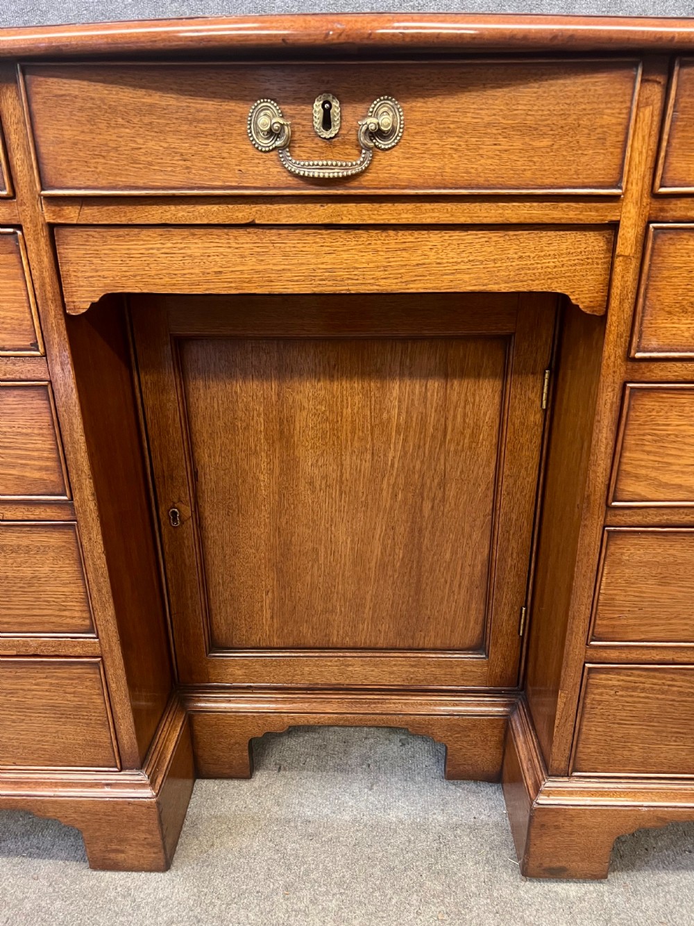 A George III mahogany kneehole desk featuring multiple drawers with brass swan-neck handles, a central recessed cupboard, and bracket feet. View IX