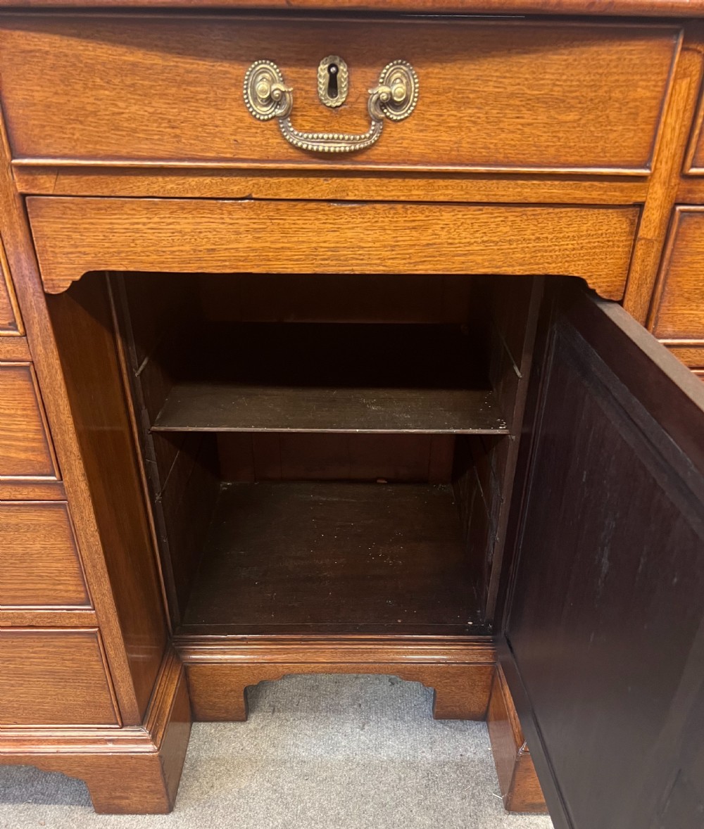 A George III mahogany kneehole desk featuring multiple drawers with brass swan-neck handles, a central recessed cupboard, and bracket feet. View X