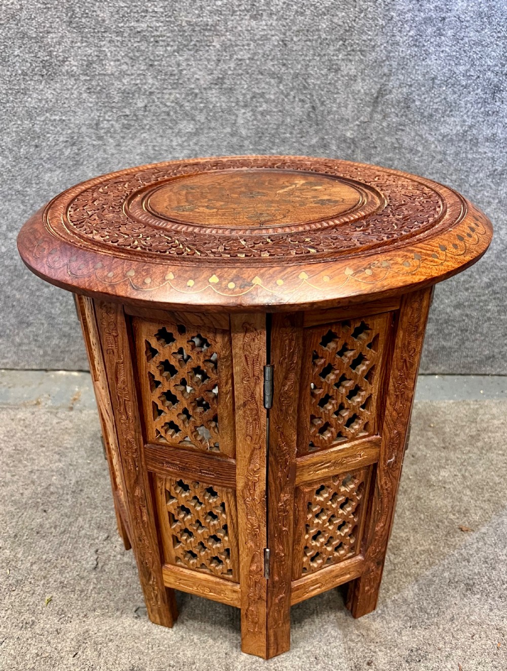 A small octagonal wooden side table featuring floral brass inlay on the top and pierced jali lattice panels on the base.