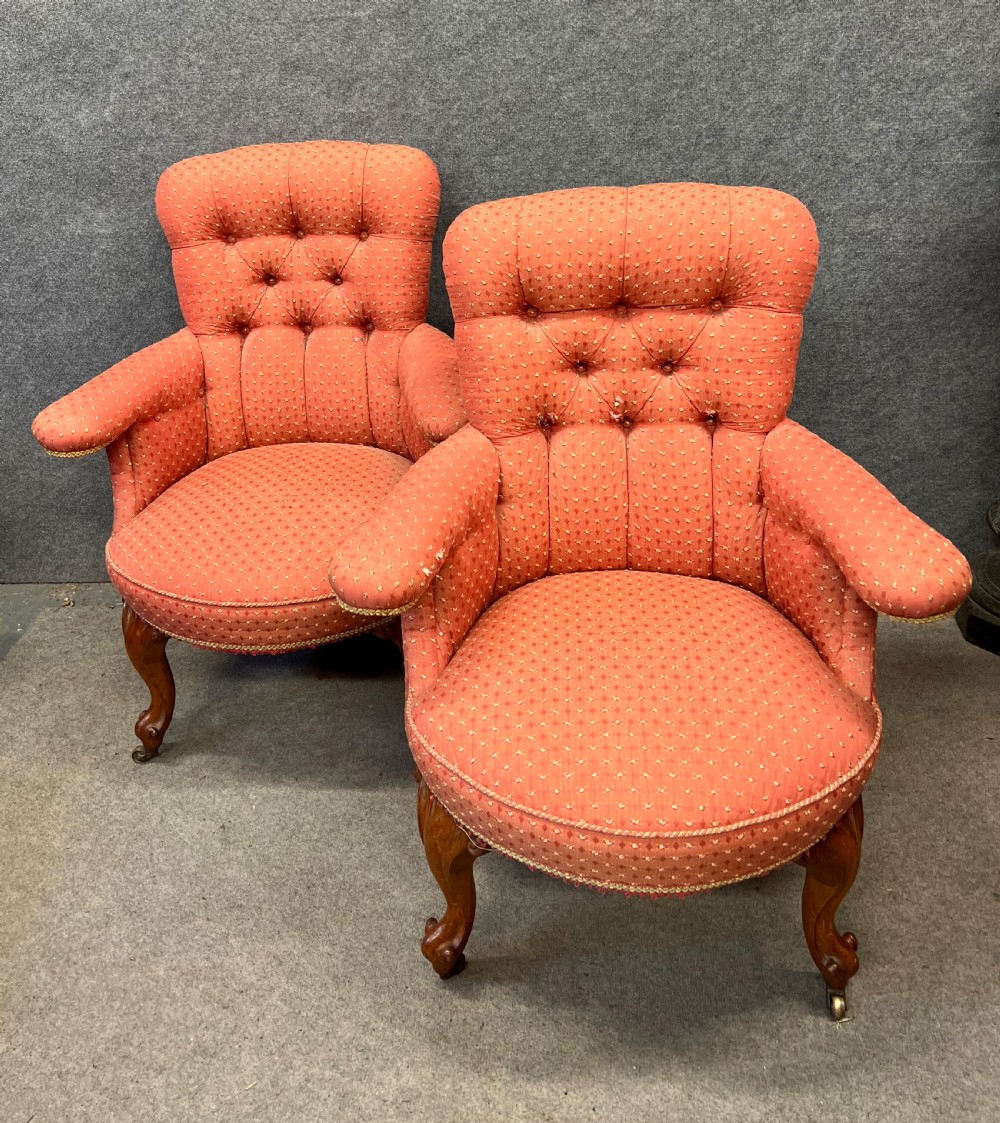 A pair of Victorian tub armchairs featuring patterned terracotta fabric, deep button tufting, and carved timber cabriole legs with brass castors.