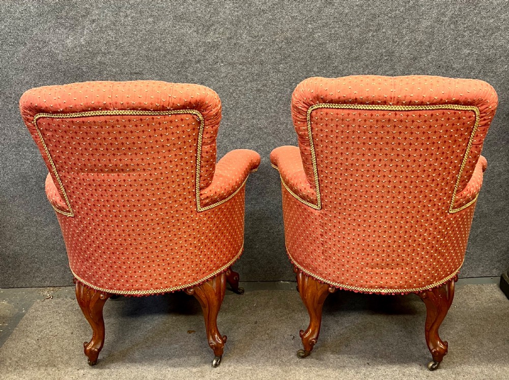 A pair of Victorian tub armchairs featuring patterned terracotta fabric, deep button tufting, and carved timber cabriole legs with brass castors. View V